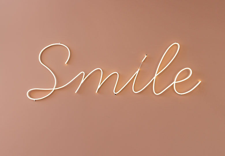 Das Wort "Smile" mit Leuchtschriftlogo vor einem einfarbigen Hintergrund. 