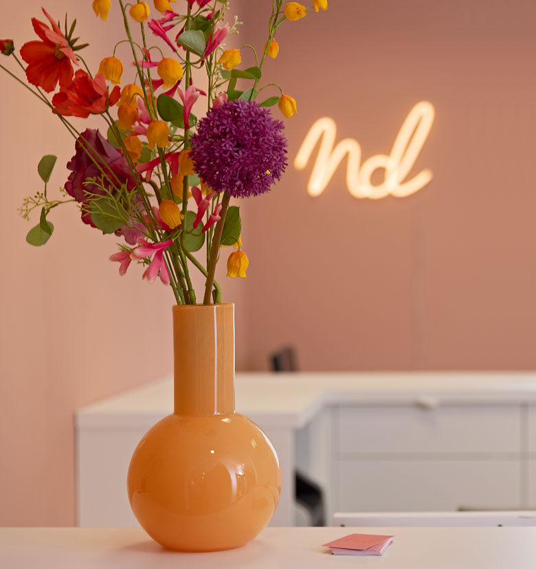 Blumen in einer Orangenen Vase vor dem "nd" Logo im Leuchtschrift. 